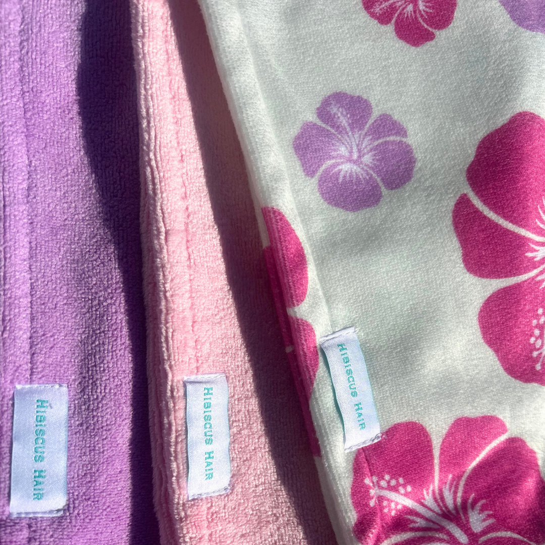 Three fabric hair extensions by Hibiscus Hair shown in a close-up diagonal arrangement. The leftmost piece is a solid lavender-purple terry cloth.