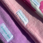 Close-up of folded fabric hair wraps in pink and purple, each with a white label reading 'Hibiscus Hair'.